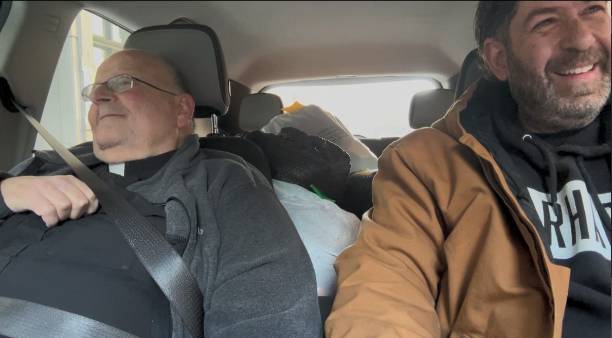 Two men in a car, one sleeping and the other driving.