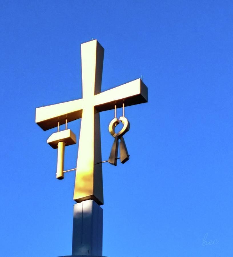 Metal cross sculpture against a clear blue sky.