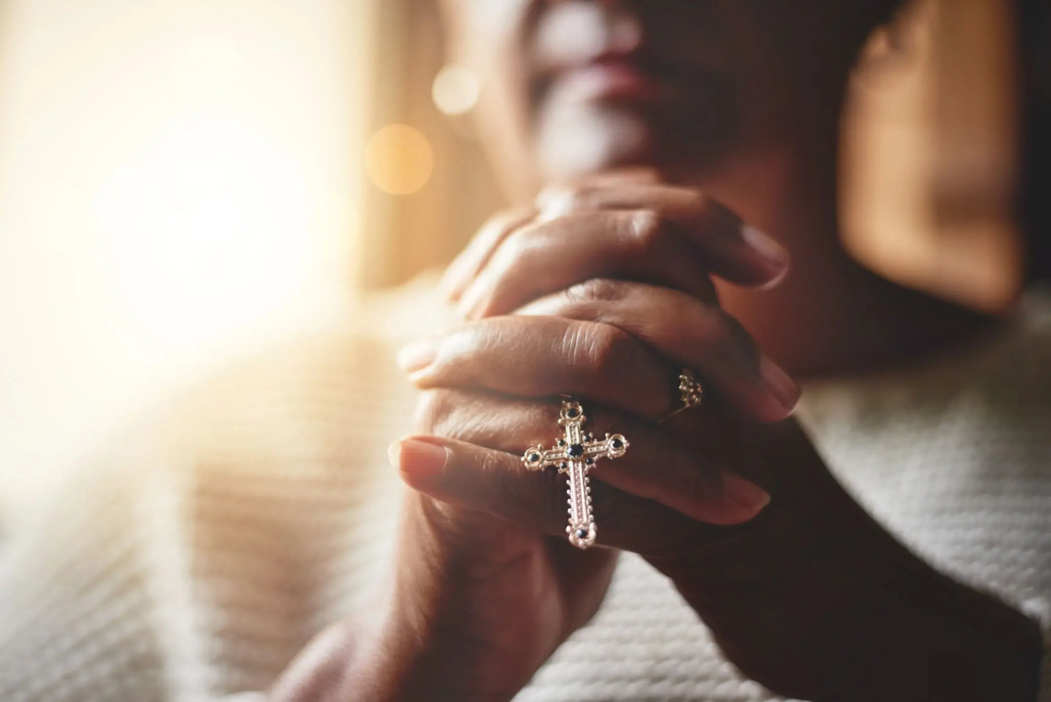 Person holding a rosary with a cross pendant in prayer.